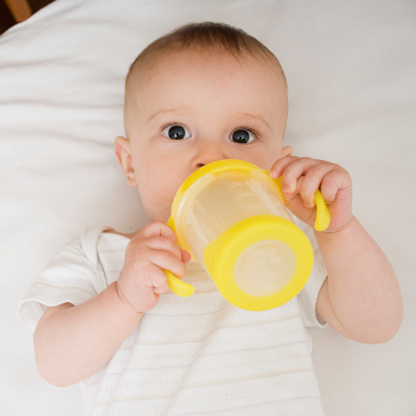 Baby lying down and drinking from a yellow sippy cup