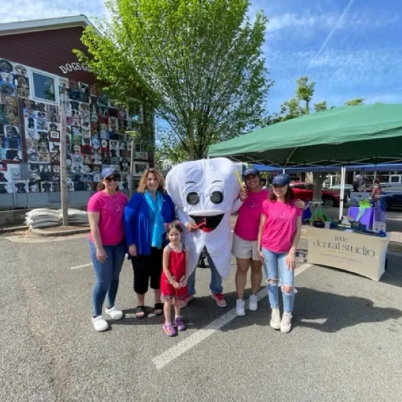 Little Dental Studio team gathered outdoors at a community event with a large smiling tooth mascot