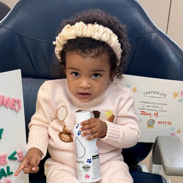 Baby sitting in a dental chair holding a toothbrush and paperwork during a dental visit
