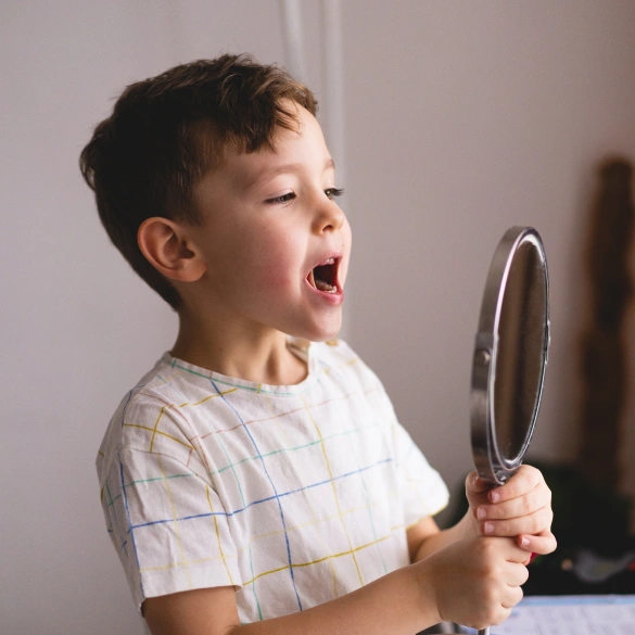 Young boy with mouth open wide holding a mirror during a dental examination