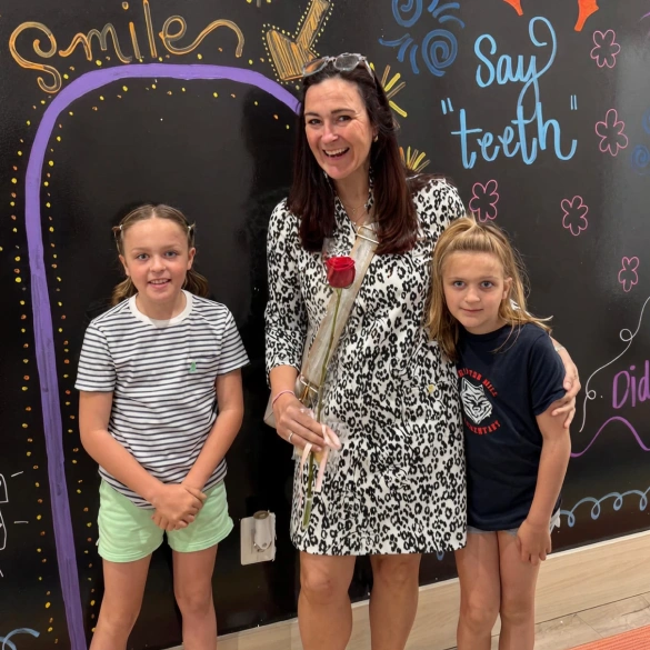 A mother posing with her two daughters in front of the Little Dental Studio smile wall mural