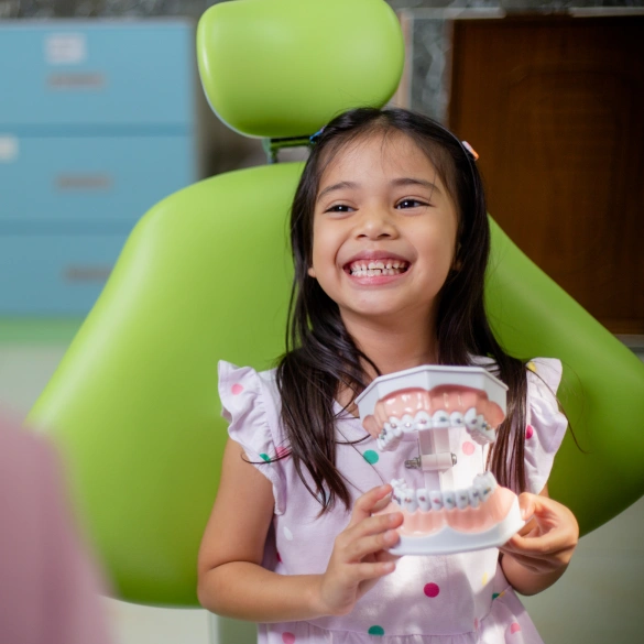 Young girl smiling and holding a dental model while seated in a dental chair