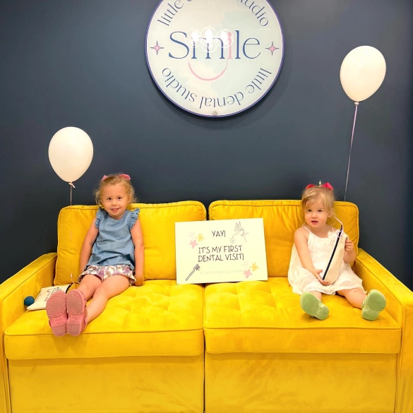 Two young children sitting on a yellow couch in the Little Dental Studio waiting room