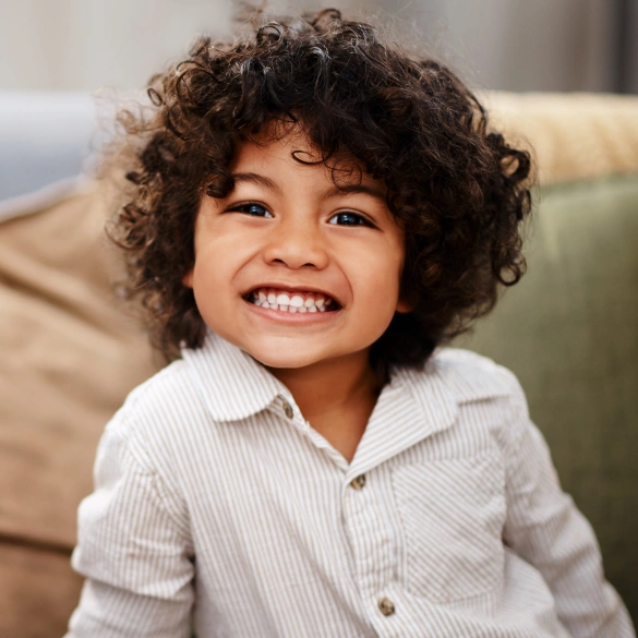 Young child with curly hair smiling brightly during a dental visit