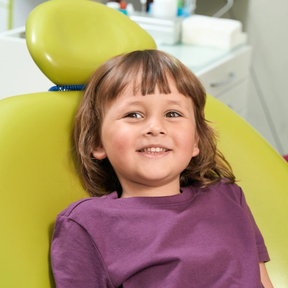 Young child smiling while seated in a green dental chair during a sedation dentistry appointment