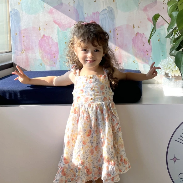 Young girl with curly hair smiling with arms outstretched inside the Little Dental Studio office