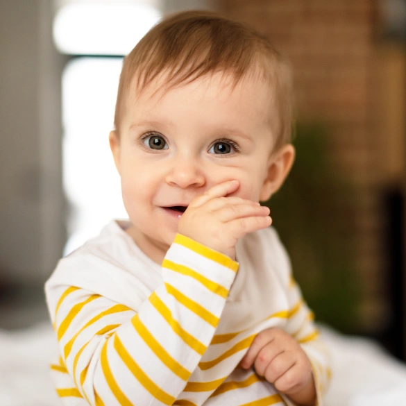 Smiling baby in a yellow striped outfit with hand near mouth